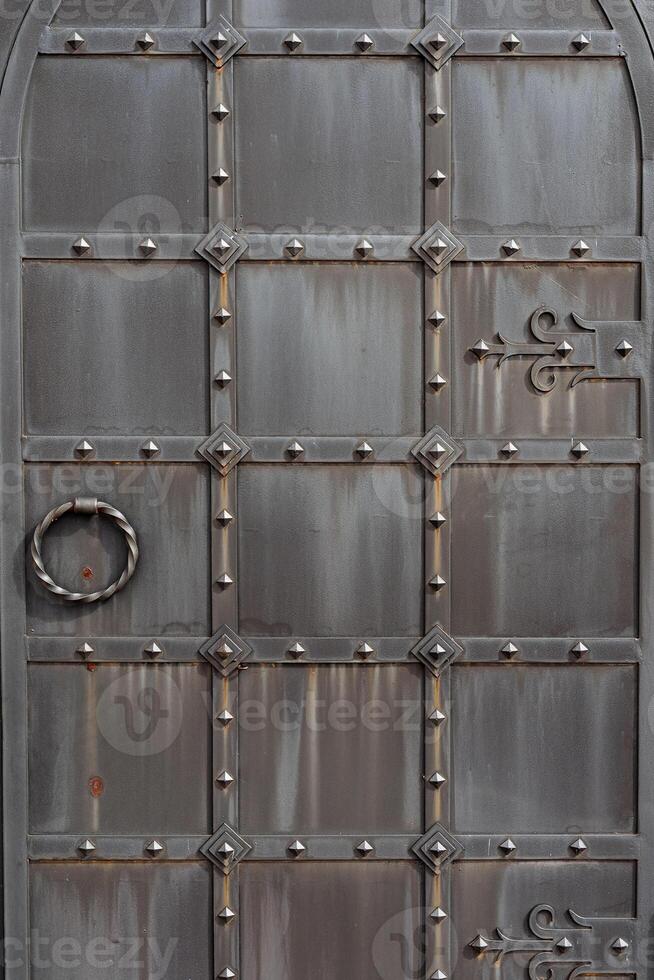 a velho metal porta, forjado portões, rebites em a fachada do uma ferro fundido porta, uma volta lidar com para aberto a porta, a textura do velho ferro. foto