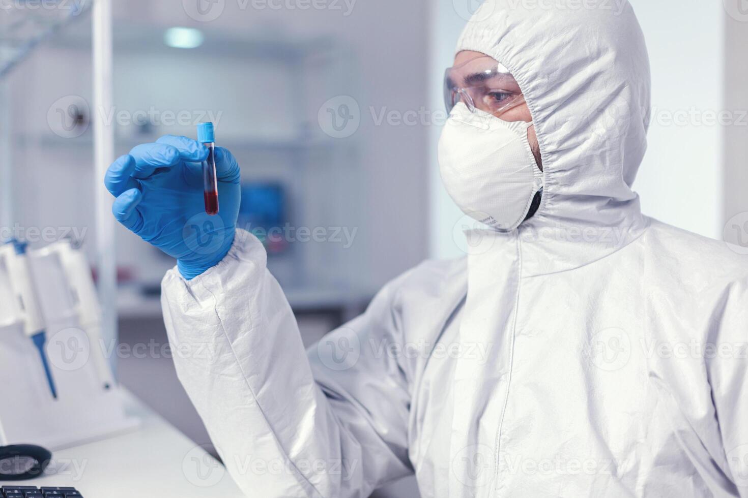 microbiologia cientistas dentro ppe terno analisar teste tubo com sangue infectado com coronavírus. médico trabalhando com vários bactérias e tecido, farmacêutico pesquisa para antibióticos contra COVID-19. foto