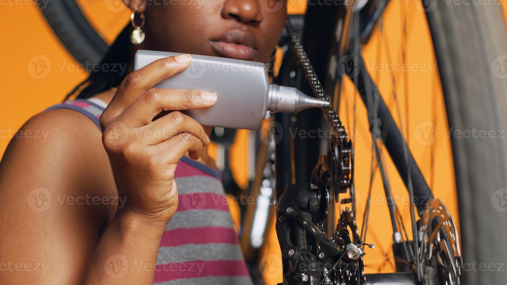 bipoc técnico usando especializado lubrificante para reparar estridente bicicleta corrente, laranja estúdio fundo. especialista aplicando óleo em barulhento bicicleta partes durante manutenção processo, fechar acima tiro foto