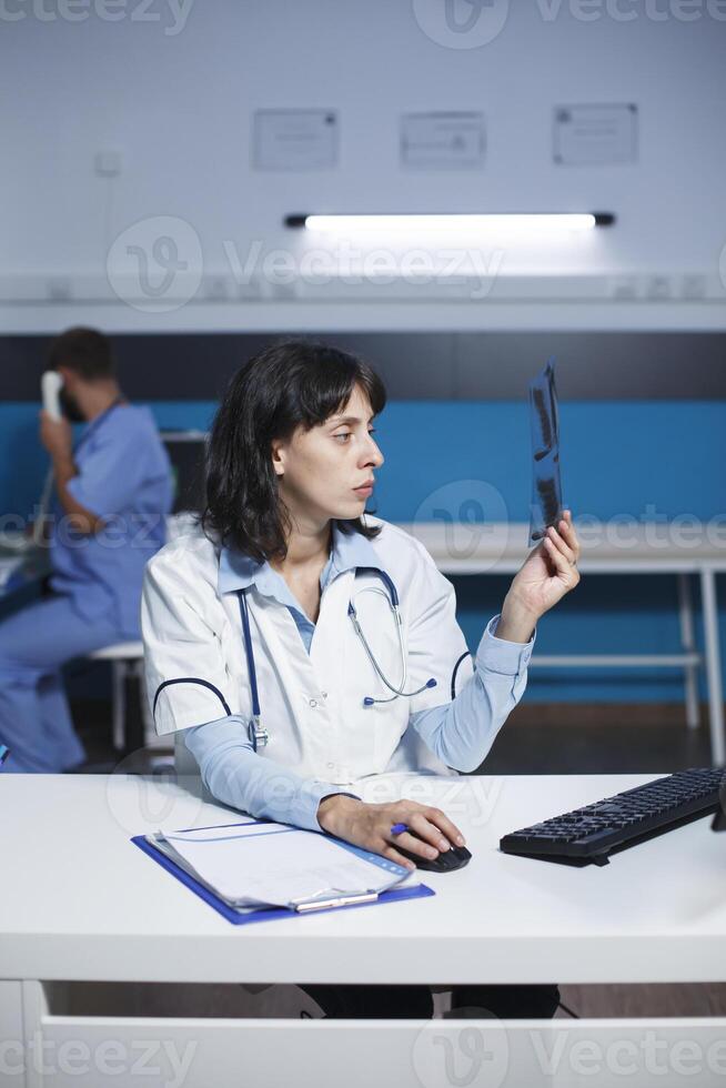 médico segurando uma radiografia analisando pulmões perícia, digitando uma médico relatório em computador, e arranjo saúde Cuidado terapia para Socorro cura uma paciente. médico trabalhando hora extra dentro a hospital escritório foto