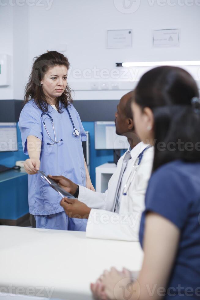 africano americano médico e caucasiano enfermeira consultando com uma fêmea paciente, fornecendo especialista adendo e exame dentro uma hospital sala. comunicação e cuidados de saúde perícia em mostrar. foto