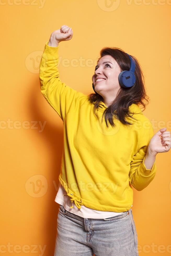 feliz pessoa dançando e ouvindo para música em fones de ouvido dentro estúdio. positivo mulher sentindo-me relaxado e fazendo dança movimentos enquanto usando fone de ouvido para apreciar sons e música sobre laranja fundo. foto