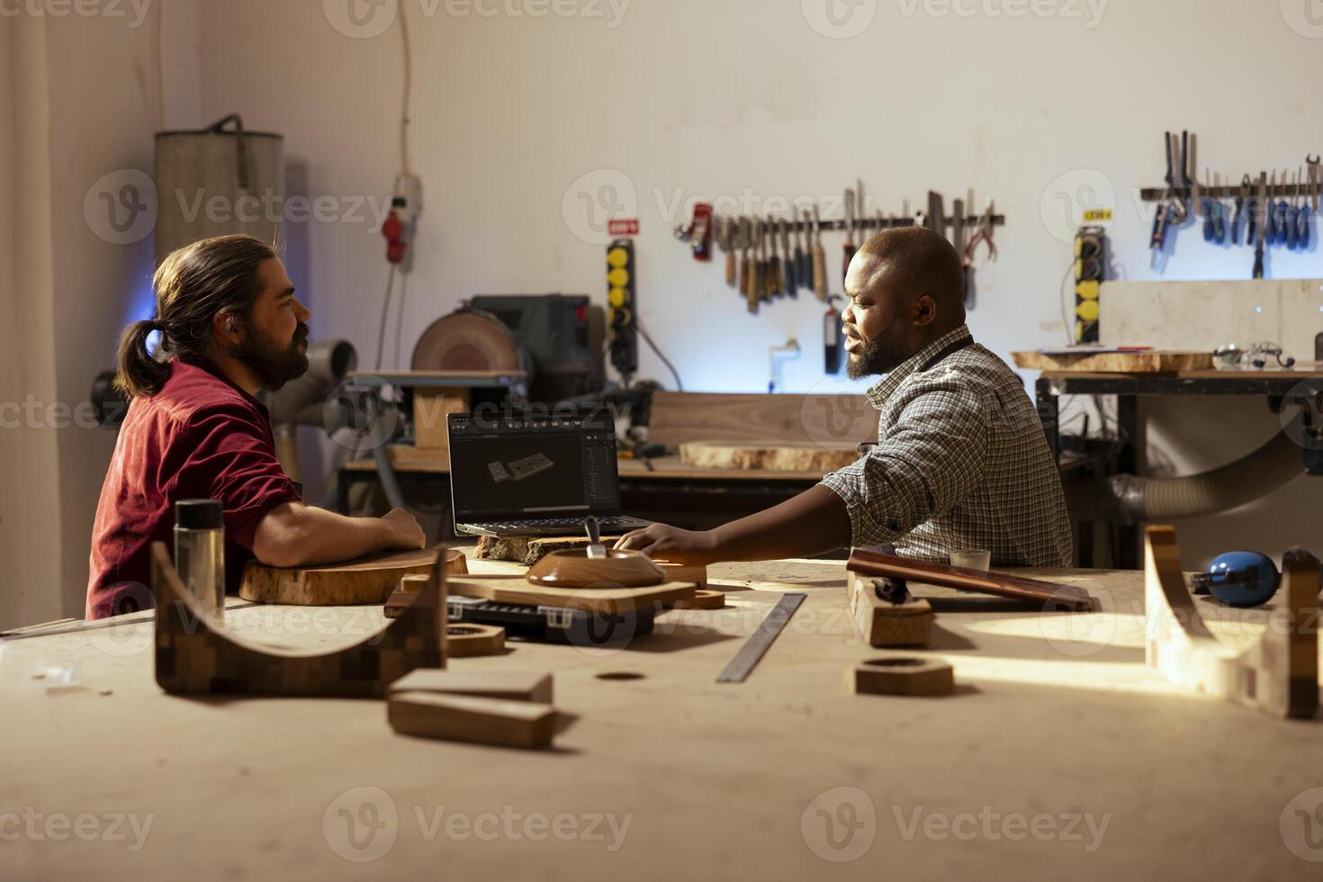 marceneiro e bipoc colega de trabalho usando cafajeste Programas em computador portátil para Projeto de madeira objetos. carpinteiro e africano americano homem usando programa em caderno para plano mobília montagem dentro marcenaria foto