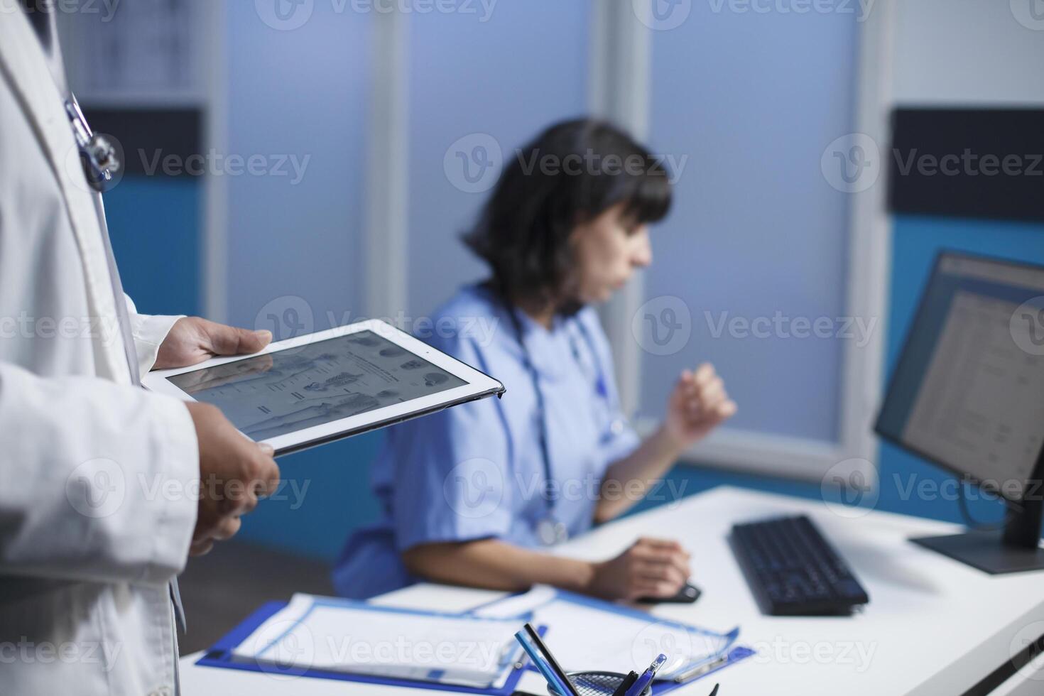 fechar-se tiro do médico profissionais utilizando moderno tecnologia para discutindo cuidados de saúde dentro uma clínica. seletivo foco mostra uma pessoa segurando uma tábua e uma fêmea enfermeira usando uma computador. foto