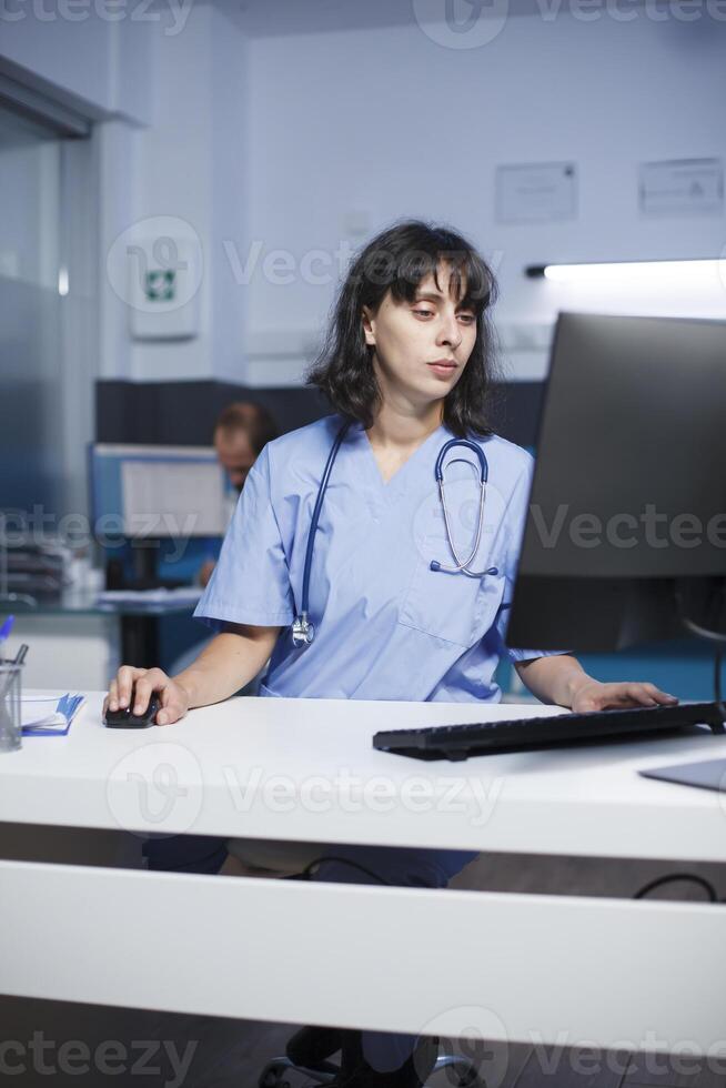 dentro clínica escritório, comprometido médico usando computador para analisar paciente registros. fêmea enfermeira verificação paciente em formação em uma Área de Trabalho computador dentro a hospital com focado atenção. foto