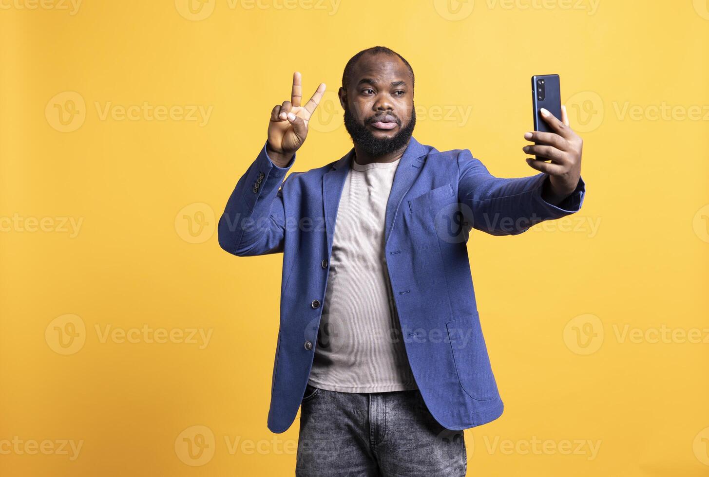 homem usando Smartphone para levar selfies, fazendo vitória mão placa. africano americano pessoa levando fotos usando telefone selfie Câmera, mostrando Paz símbolo gesticulando, estúdio fundo