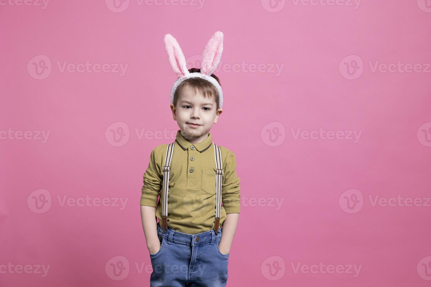 jovem alegre criança vestindo fofa Coelho orelhas dentro frente do Câmera, sentindo-me animado sobre Páscoa evento festividade e em pé contra Rosa fundo. alegre pequeno Garoto com adorável roupa. foto