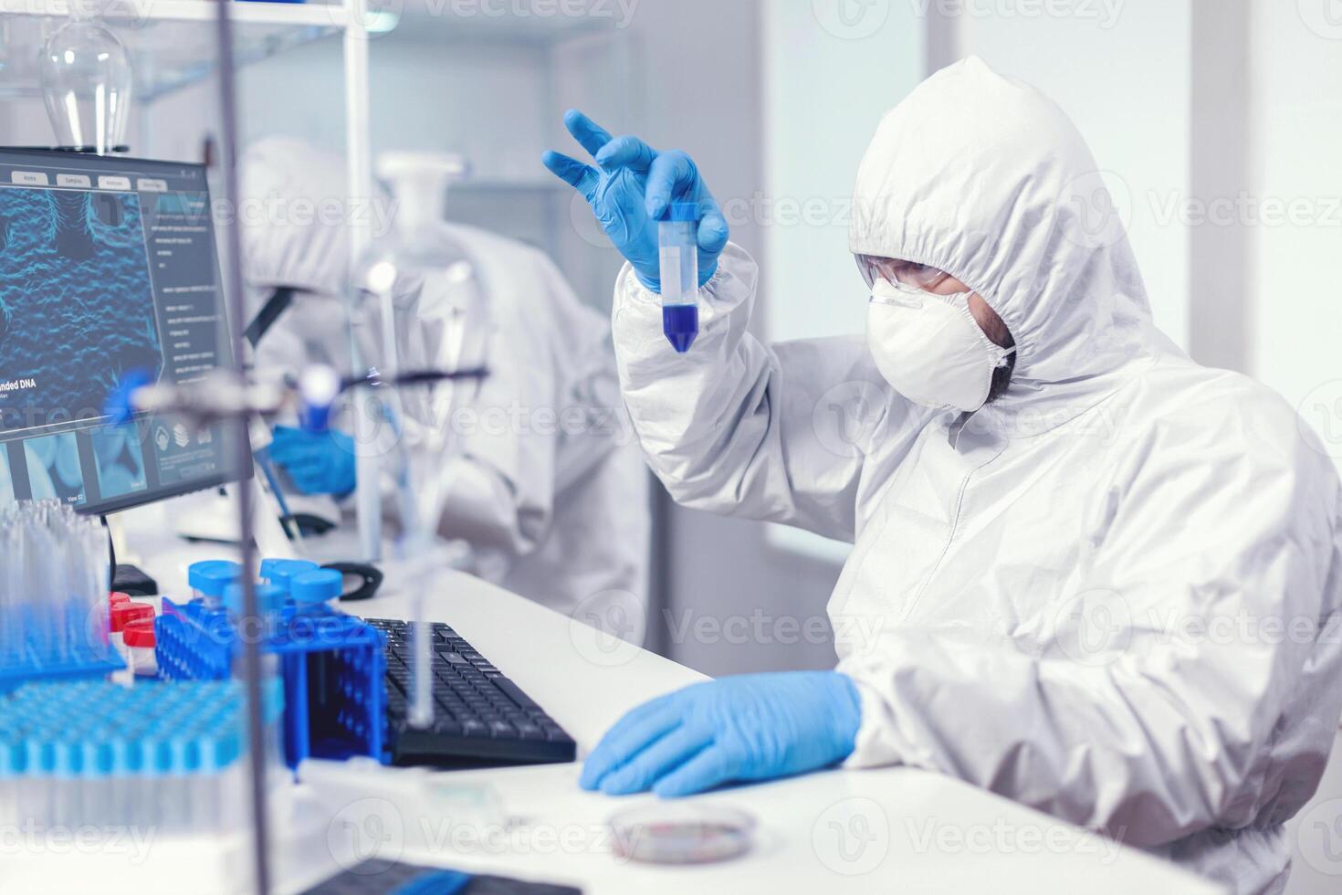 cientista dentro laboratório macacão olhando de perto às amostra dentro teste tubo dentro a curso do coroavírus. investigador dentro laboratório vestindo macacão fazendo pesquisa e analisando substância durante global pandemia com COVID-19. foto