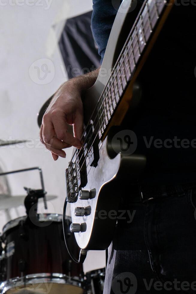 uma homem jogando uma graves guitarra dentro uma casual contexto. ele é focado em dele instrumento, dedos planador sobre a cordas. dele relaxado postura e casual vestuário sugerir uma descontraído música sessão. foto