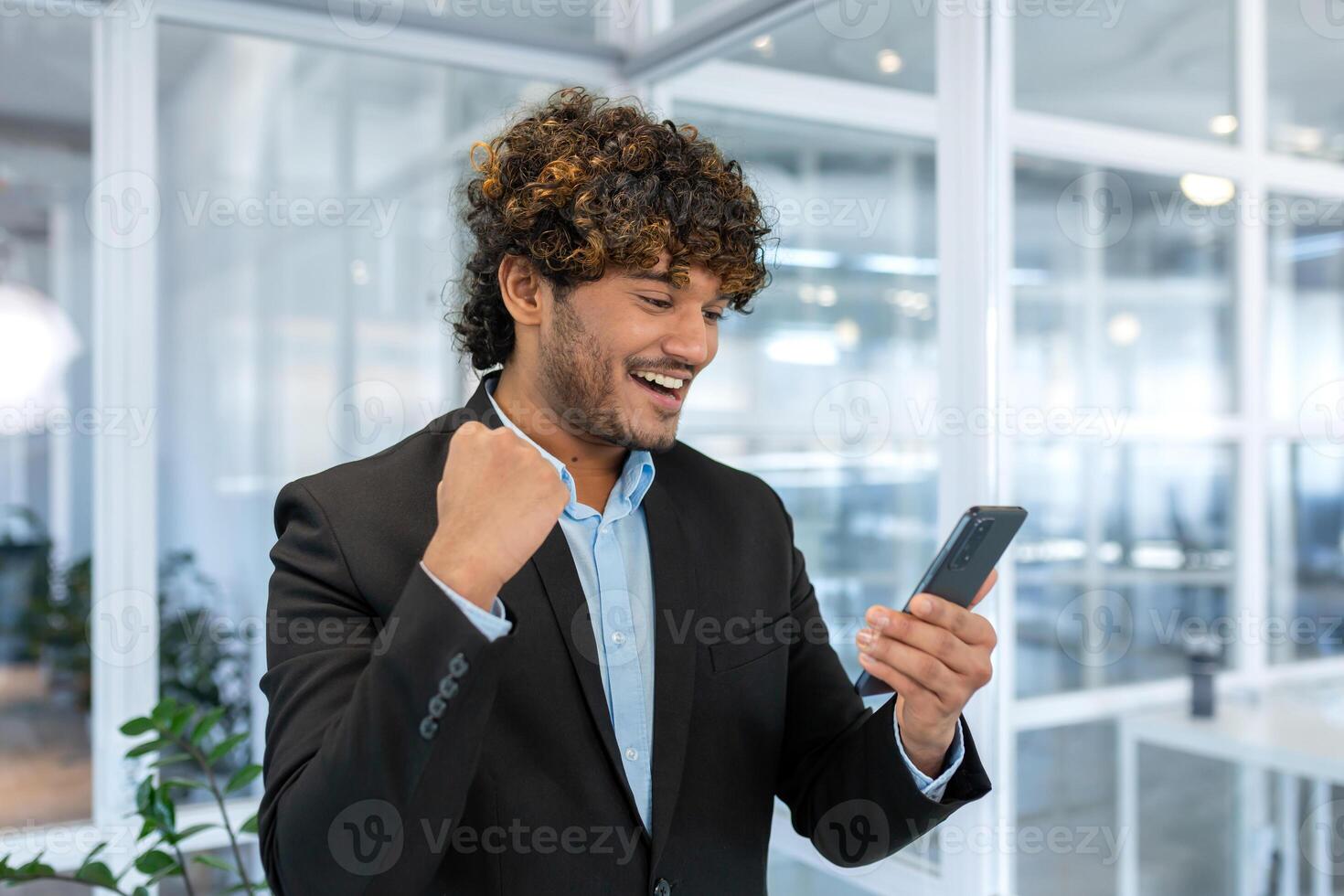 bem sucedido hispânico patrão perto janela recebido Boa notícia on-line, homem de negocios usar telefone e comemoro vitória e Boa realização resultados dentro escritório, homem dentro camisa excitadamente alegrar. foto