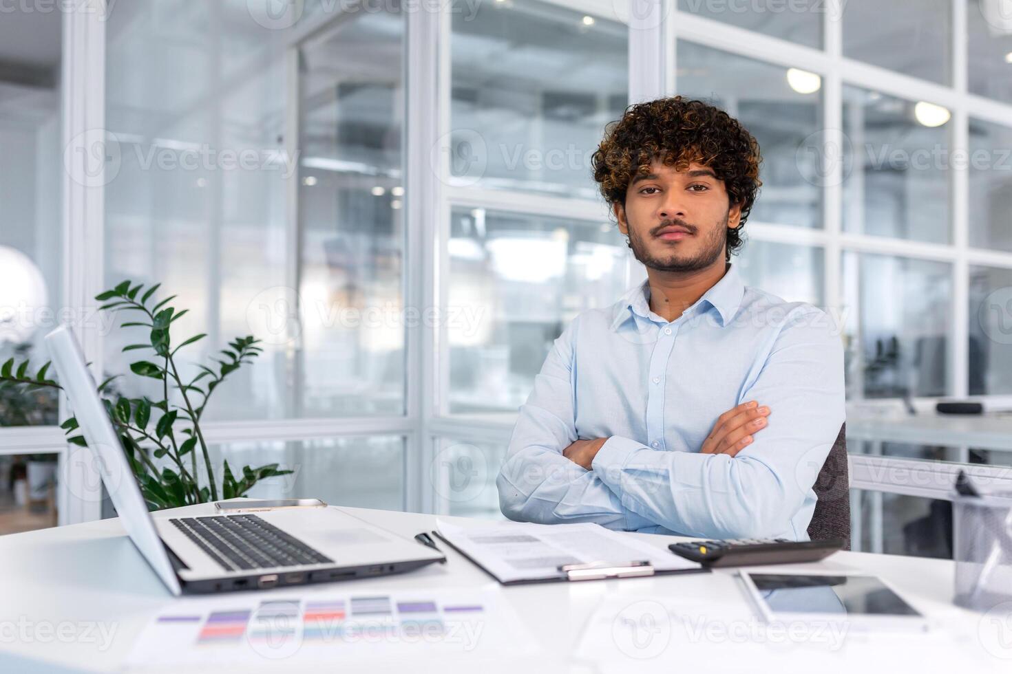 retrato do sério e confiante financista homem de negocios com cruzado braços pensando olhando às Câmera, bem sucedido hispânico homem trabalhando dentro financeiro companhia escritório com documentos, usando calculadora foto