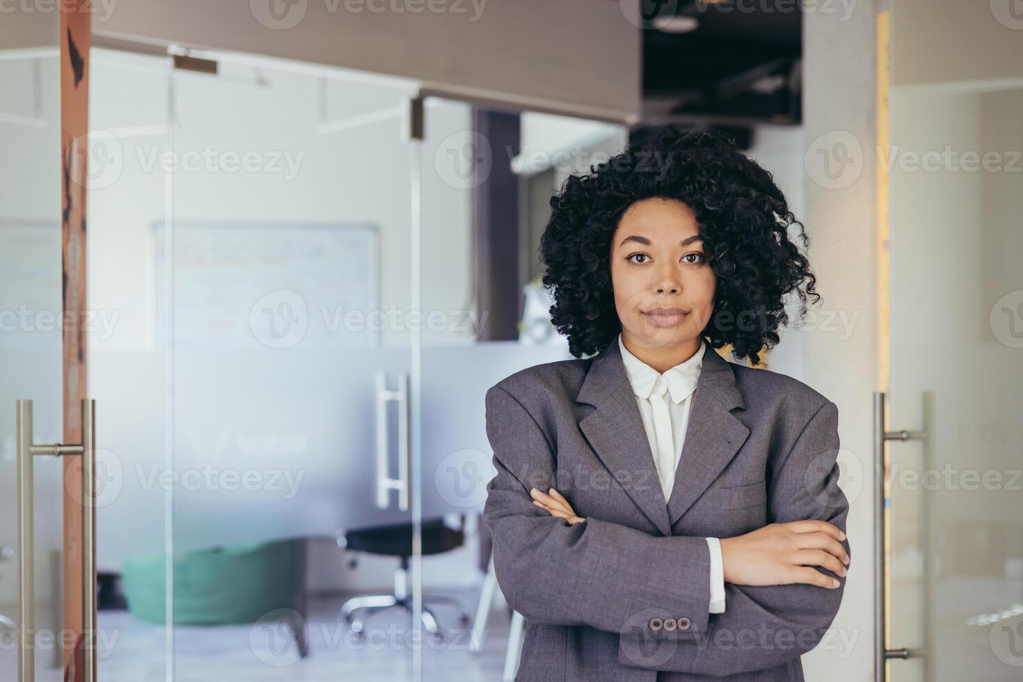 retrato do sério fêmea patrão dentro o negócio companhia escritório, empresária cruzado braços olhando concentrado às Câmera, vestindo camisa, satisfeito e bem sucedido mulher com encaracolado cabelo. foto