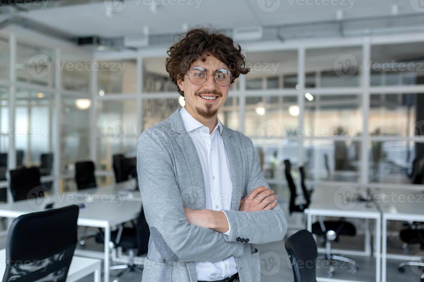 retrato do uma jovem maduro masculino profissional com encaracolado cabelo com confiança em pé dentro uma bem iluminado corporativo escritório. foto