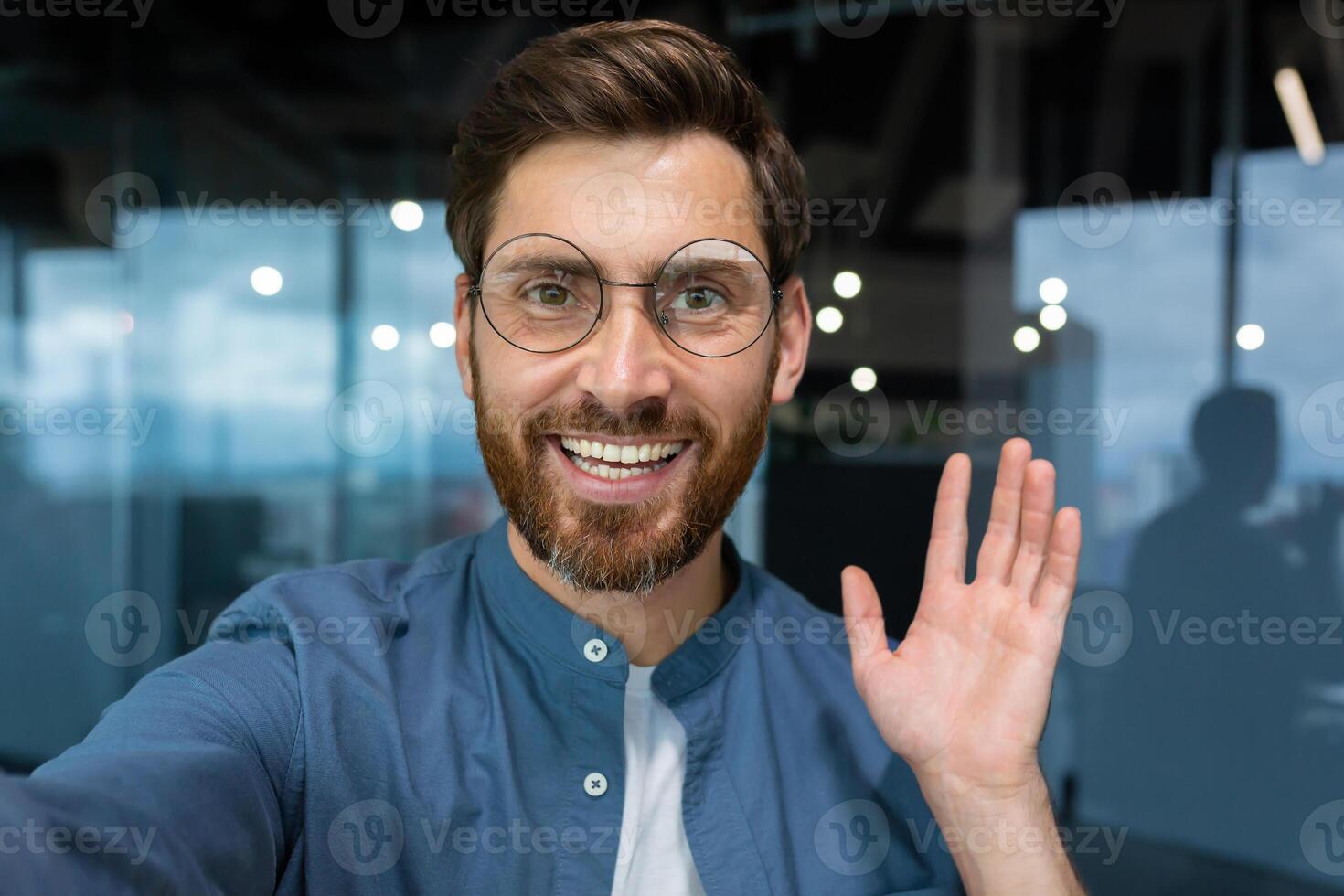 retrato do bem sucedido homem de negocios dentro casual camisa e óculos homem olhando às Smartphone Câmera e sorridente, Câmera Visão ligar falando com amigos dentro escritório remotamente. foto