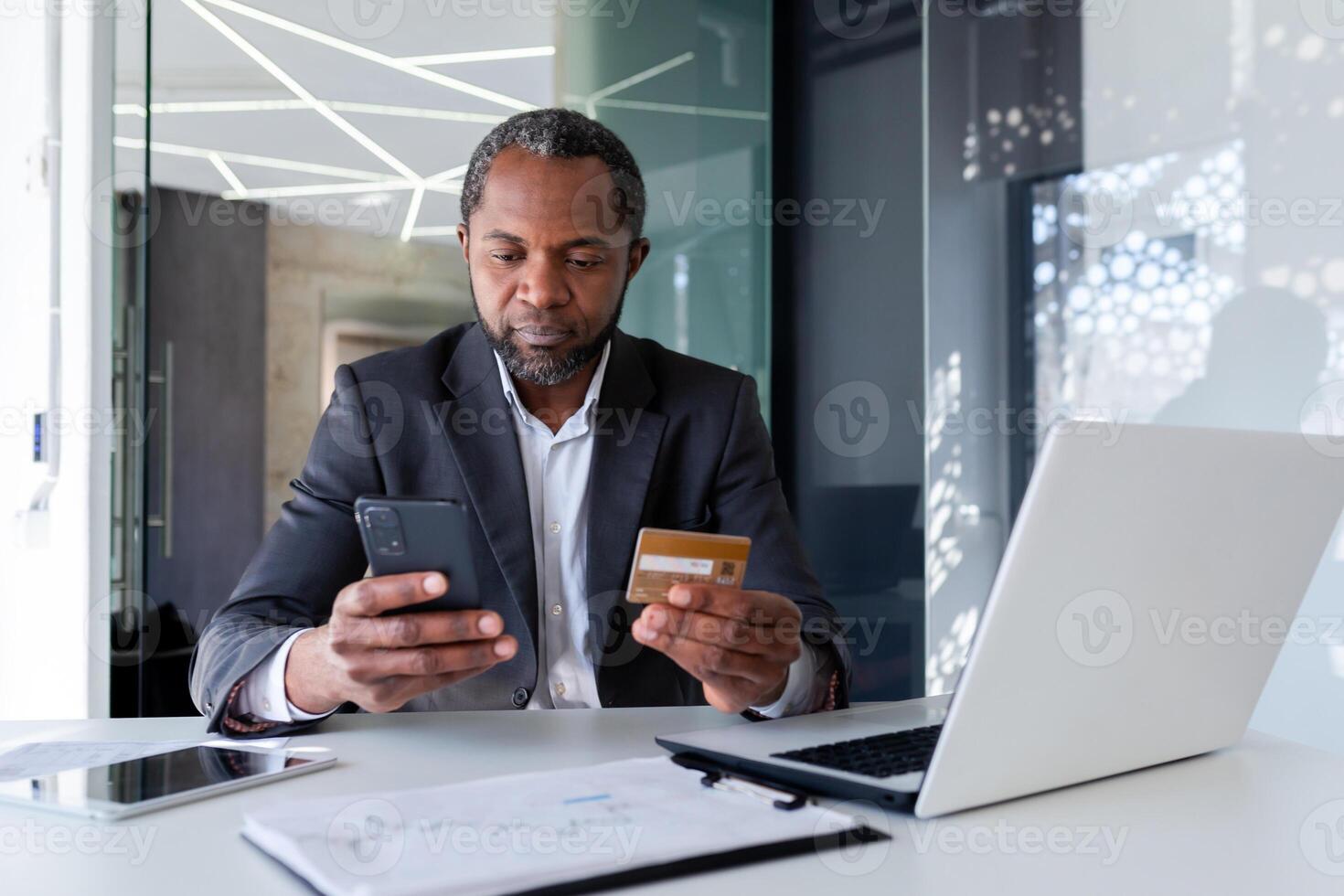 africano americano masculino empresários trabalhando dentro escritório e sentado às escrivaninha. detém e usa crédito cartão e telefone. foto