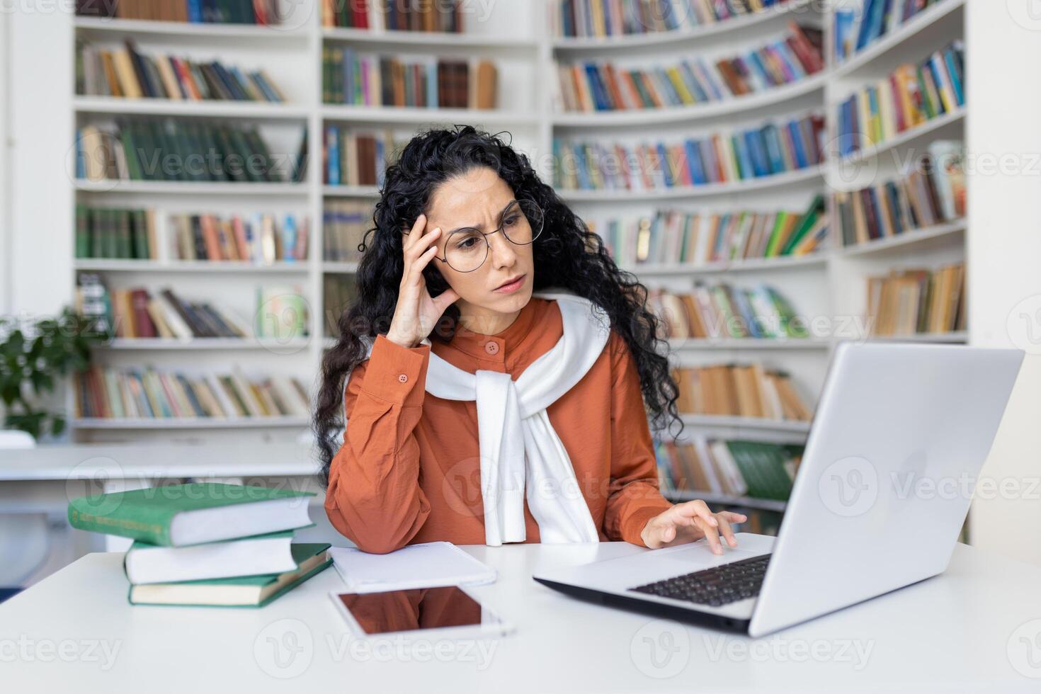 cansado jovem hispânico fêmea professor sentado às escrivaninha dentro frente do computador portátil dentro escola quarto segurando mão em cabeça, excesso de trabalho dentro escritório dor de cabeça, conectados Aprendendo conceito. foto