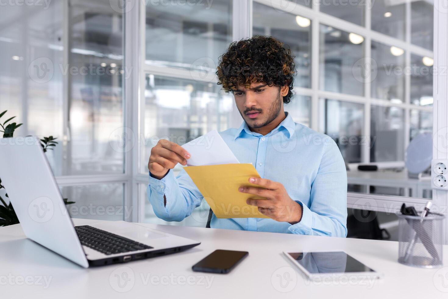 jovem homem de negocios às trabalhos dentro escritório recebido enviar envelope notificação mensagem com mau notícias, hispânico homem triste lendo carta documento sentado às mesa com computador portátil. foto