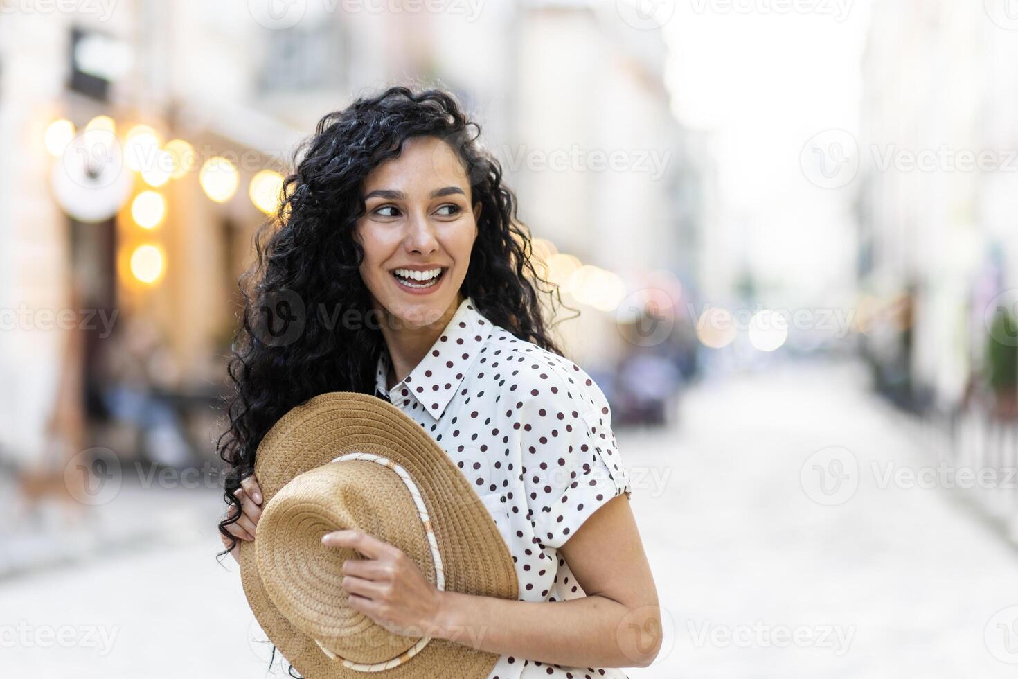 retrato do uma jovem lindo mulher dentro uma chapéu, uma turista é caminhando dentro a tarde cidade, alegremente olhando para a lado com encaracolado cabelo. foto