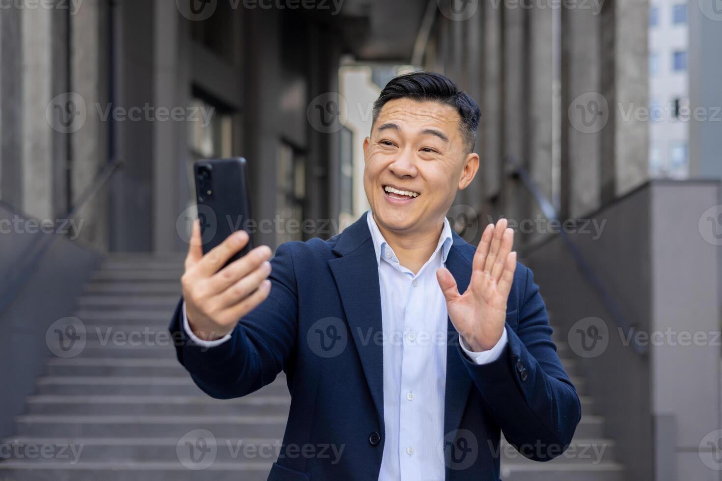 alegre ásia homem de negocios noivando dentro uma ligar usando dele Smartphone, sorridente e acenando Olá ao ar livre. foto