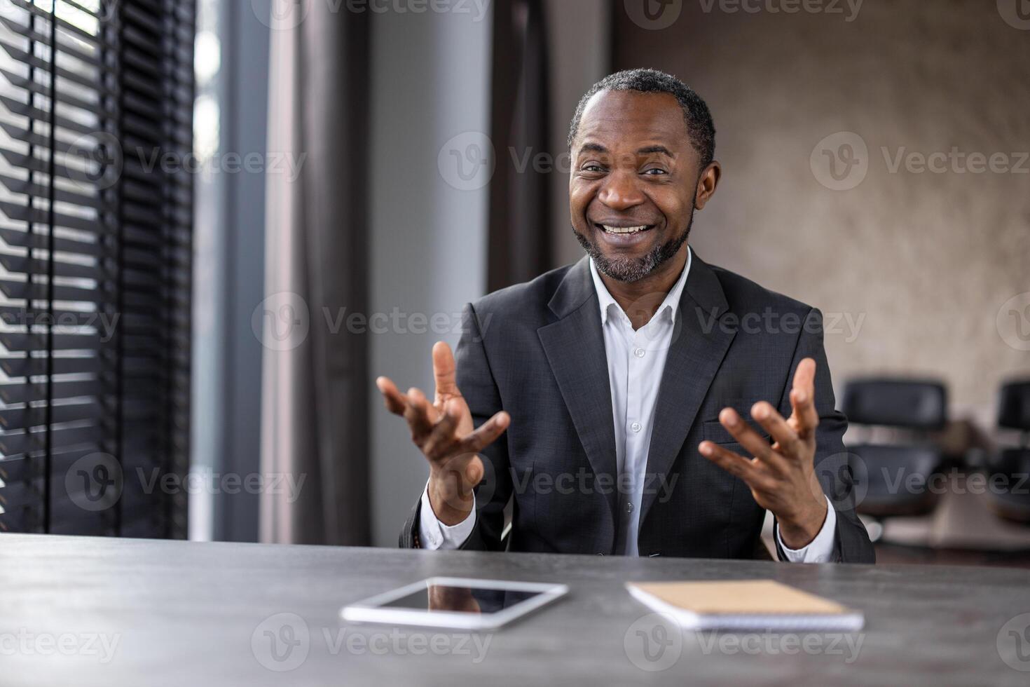 uma homem dentro uma terno é sentado às uma escrivaninha com uma tábua e uma caderno. ele é sorridente e ele é acionado dentro uma conversação foto