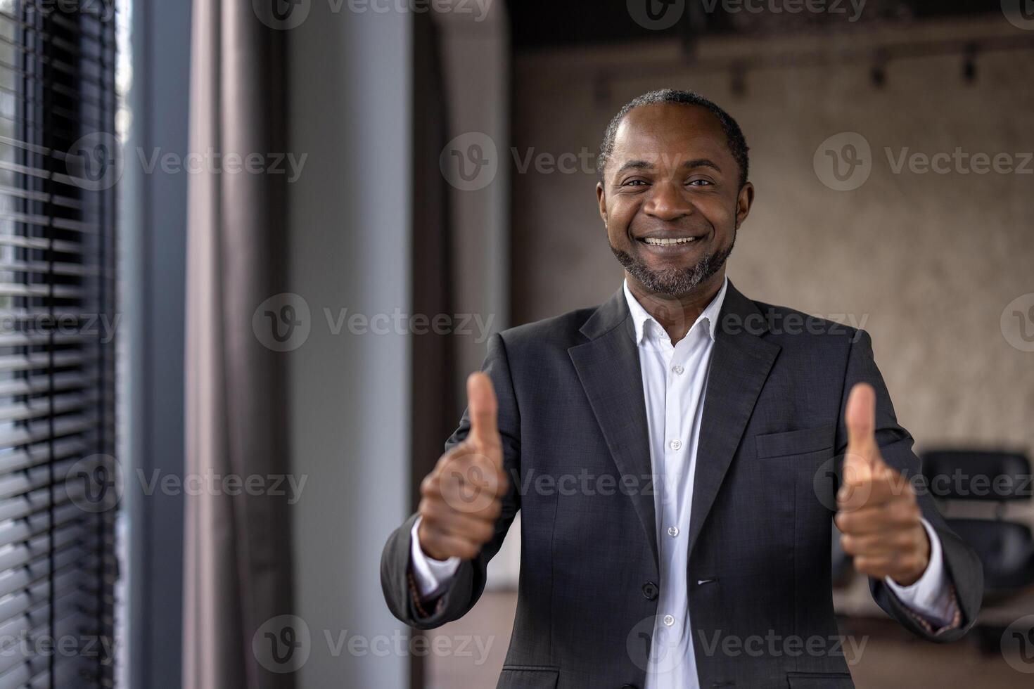 alegre africano americano homem de negocios dentro uma terno dá uma Duplo polegares acima, simbolizando aprovação e sucesso dentro a escritório ambiente. foto