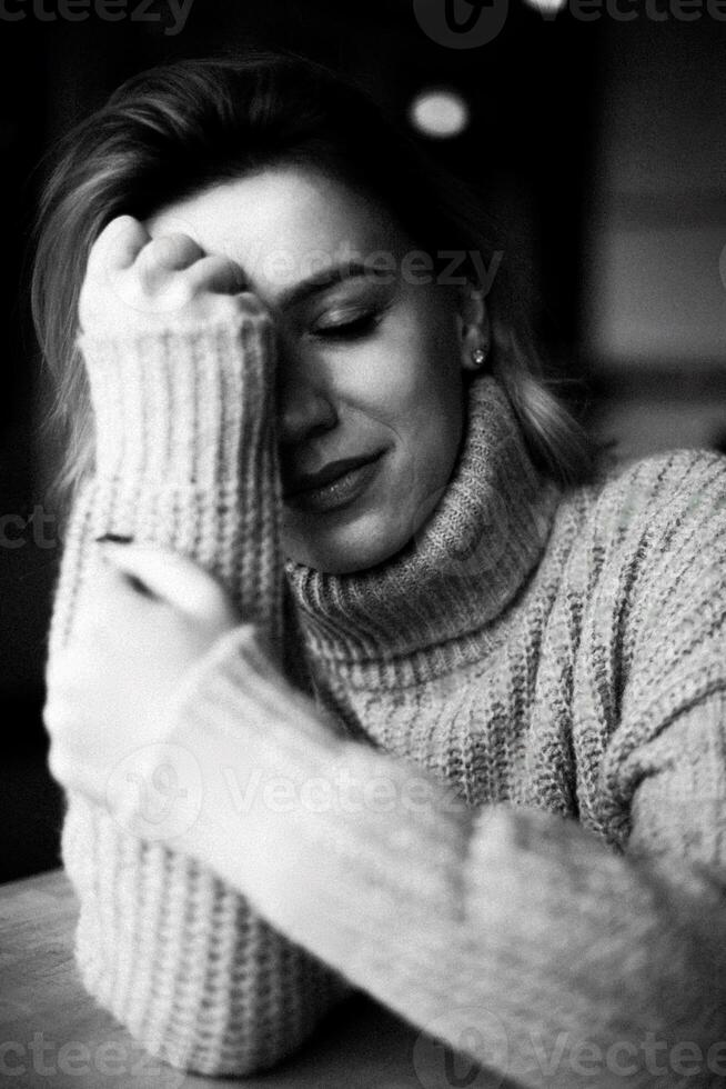 uma solitário momento capturado Como uma mulher, vestido dentro uma acolhedor suéter, senta com mãos em dela face, transmitindo uma sentido do introspecção e melancólico dentro uma sereno atmosfera foto