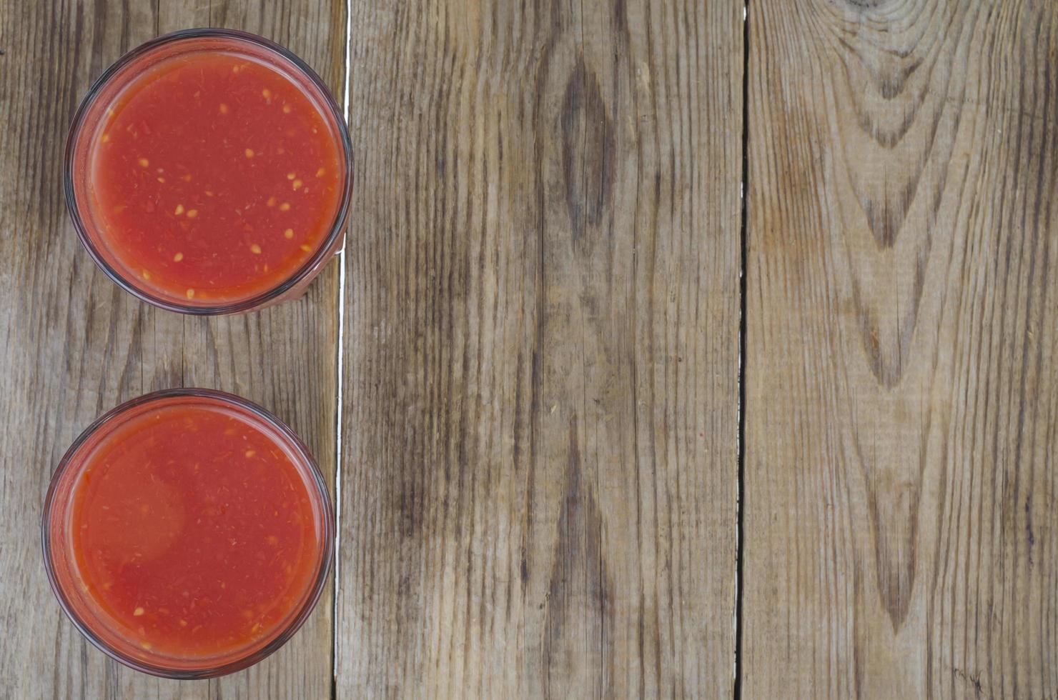copos com suco fresco de tomates vermelhos maduros na mesa de madeira foto
