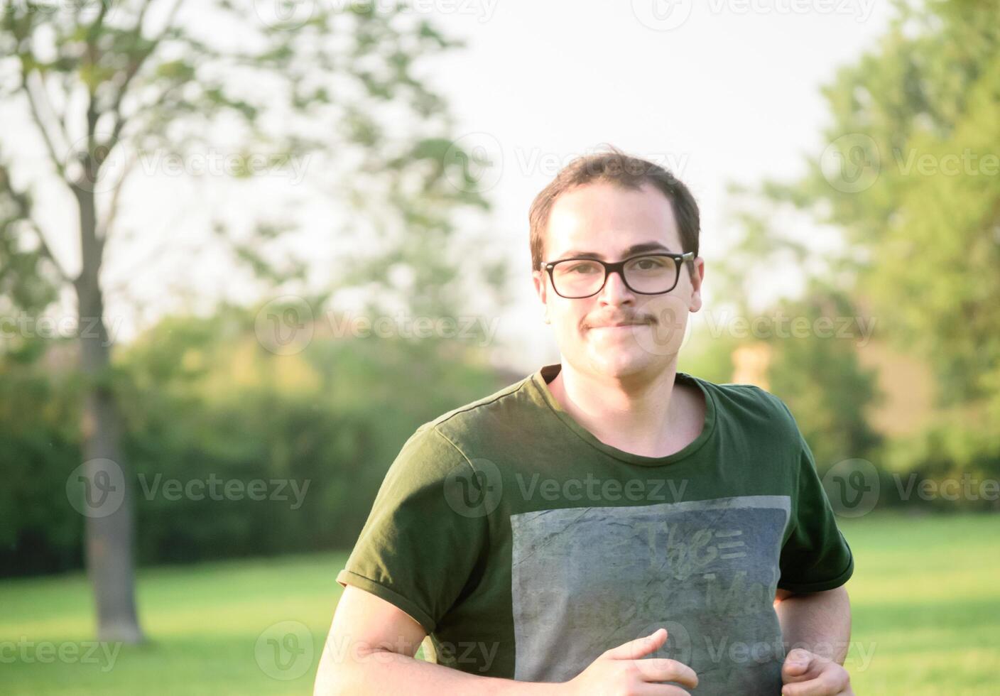 jovem homem com óculos e verde camiseta corrida dentro parque foto