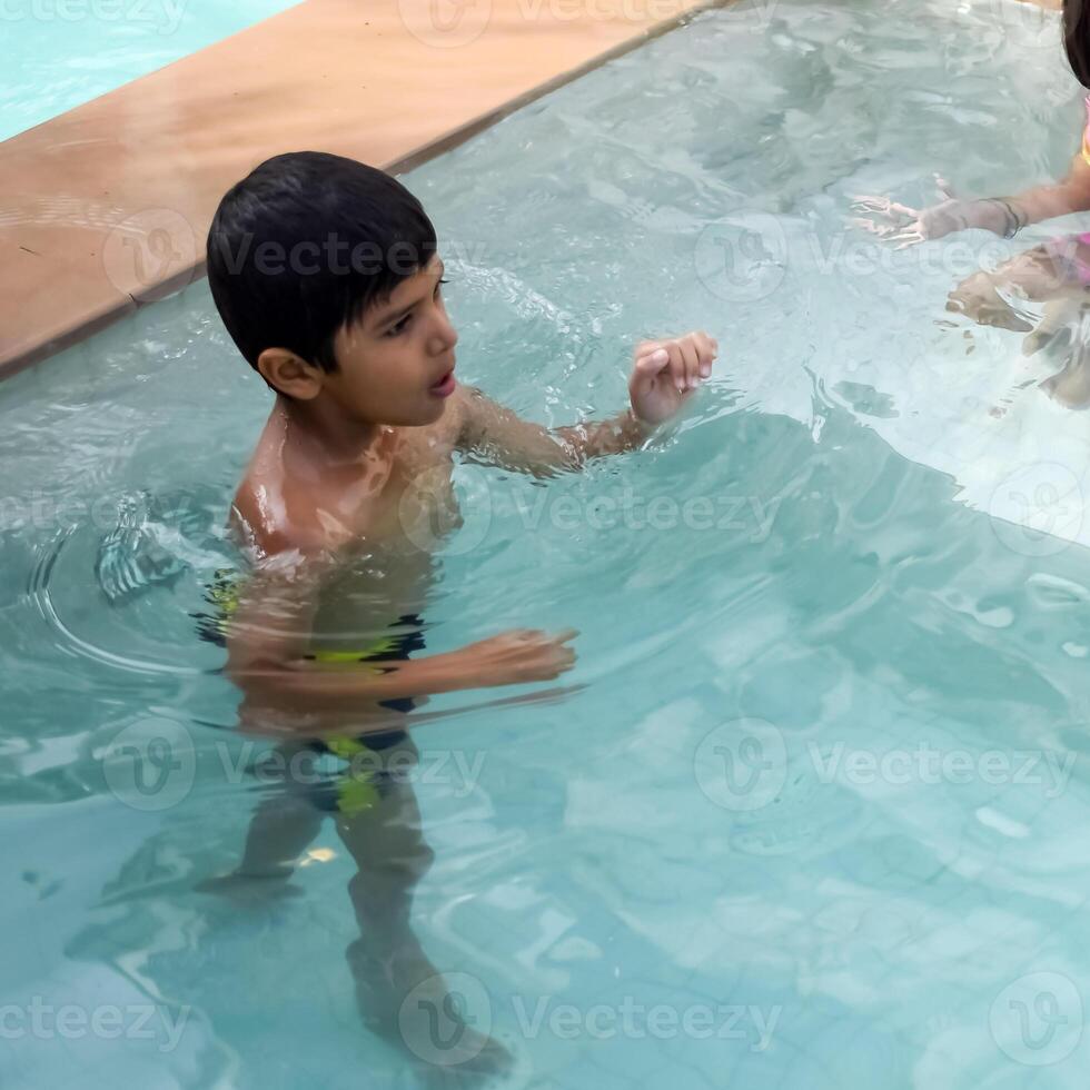 feliz indiano Garoto natação dentro uma piscina, criança vestindo natação traje ao longo com ar tubo durante quente verão Férias, crianças Garoto dentro grande natação piscina. foto