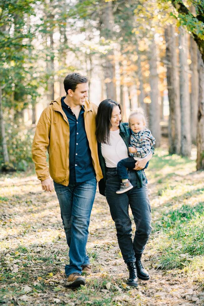 sorridente Papai abraçando mãe com uma pequeno menina dentro dela braços em uma andar foto