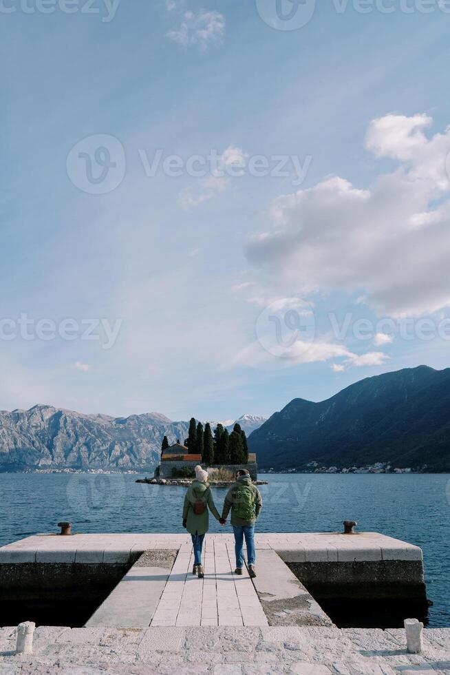 homem e mulher andar segurando mãos ao longo a cais olhando Fora sobre st. George ilha. costas visualizar. Montenegro foto