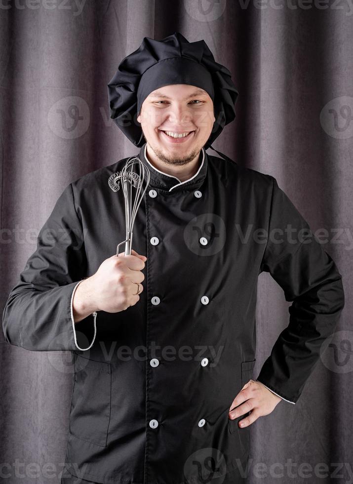 chef masculino segurando lápis de cozinha isolados no fundo da cortina escura foto