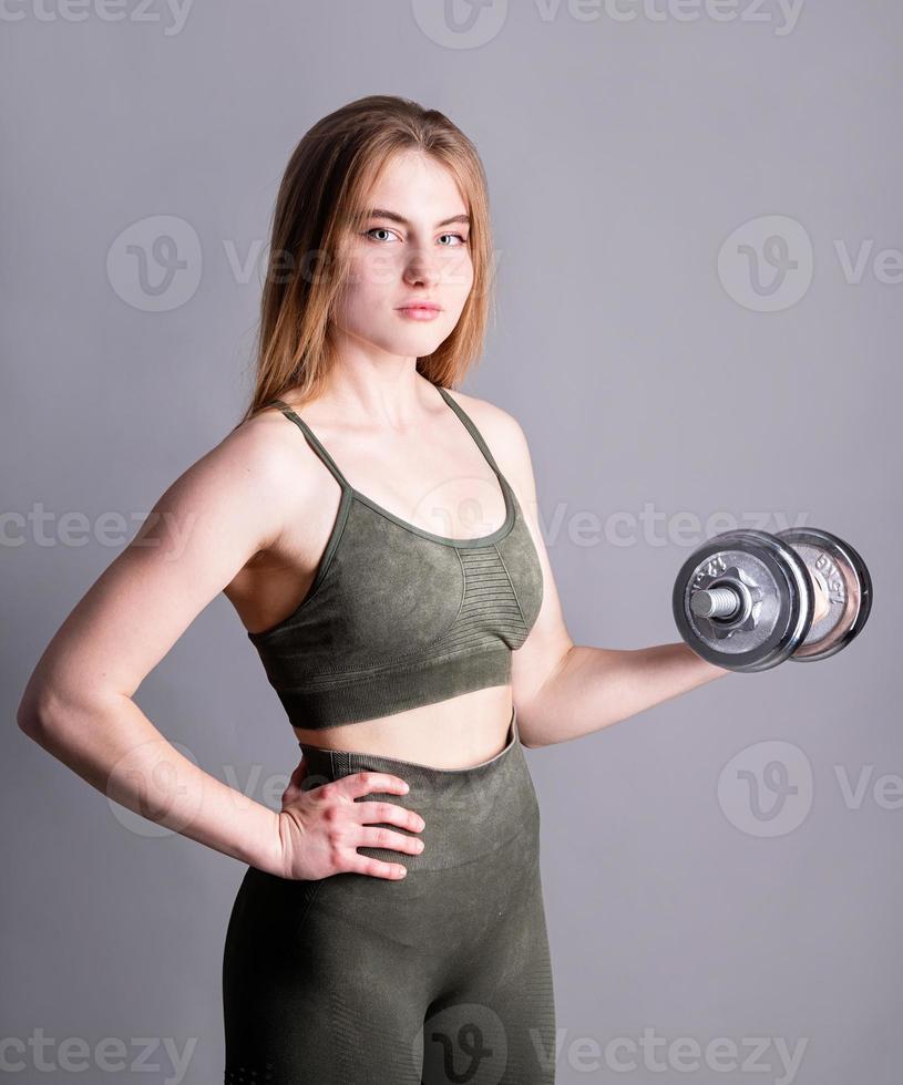 jovem mulher esportiva fazendo exercícios com halteres isolados em cinza foto