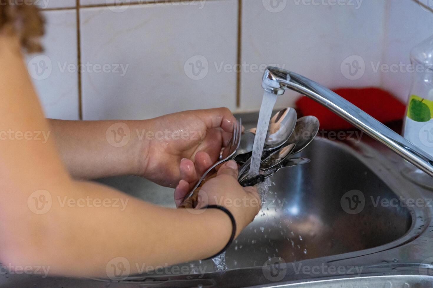 menina lavando pratos dentro Pia dentro acampamento cozinha. jovem mulher é segurando garfos e colheres enquanto lavagem eles. limpeza facas e garfos. água é fluindo e respingando com salpicos Fora do tocar. foto