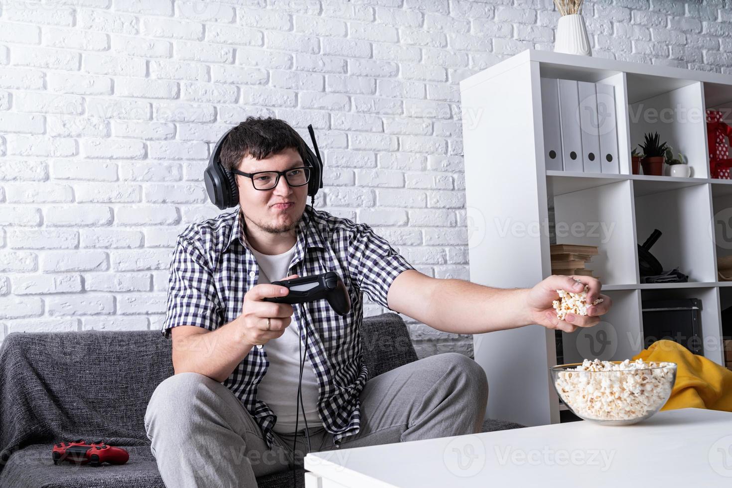 jovem jogando videogame em casa comendo pipoca foto