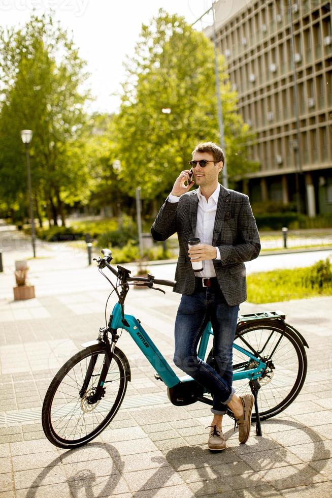 jovem empresário usando telefone celular na ebike com uma xícara de café para viagem foto