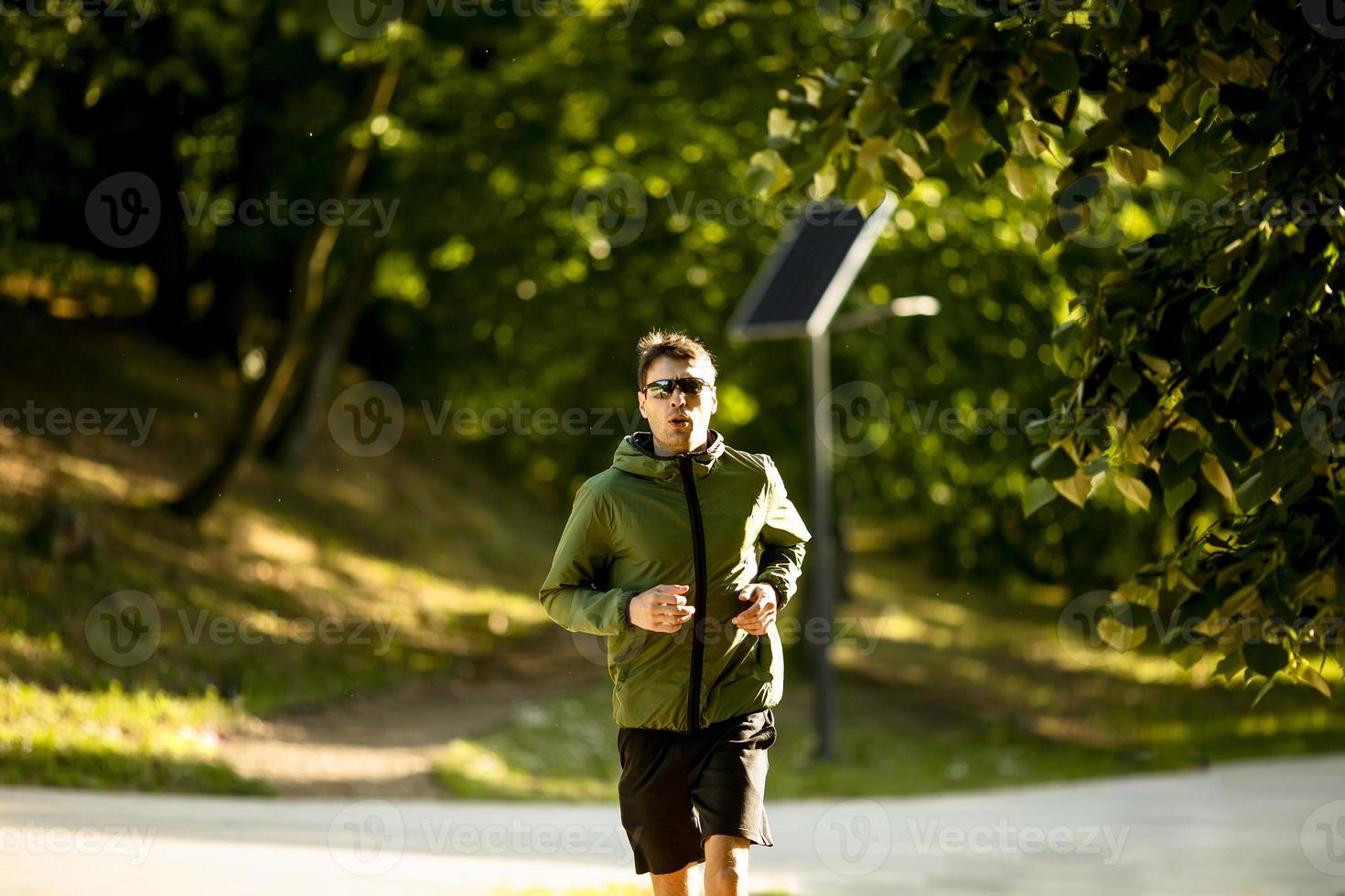 jovem atlético correndo enquanto faz exercícios no parque verde ensolarado foto