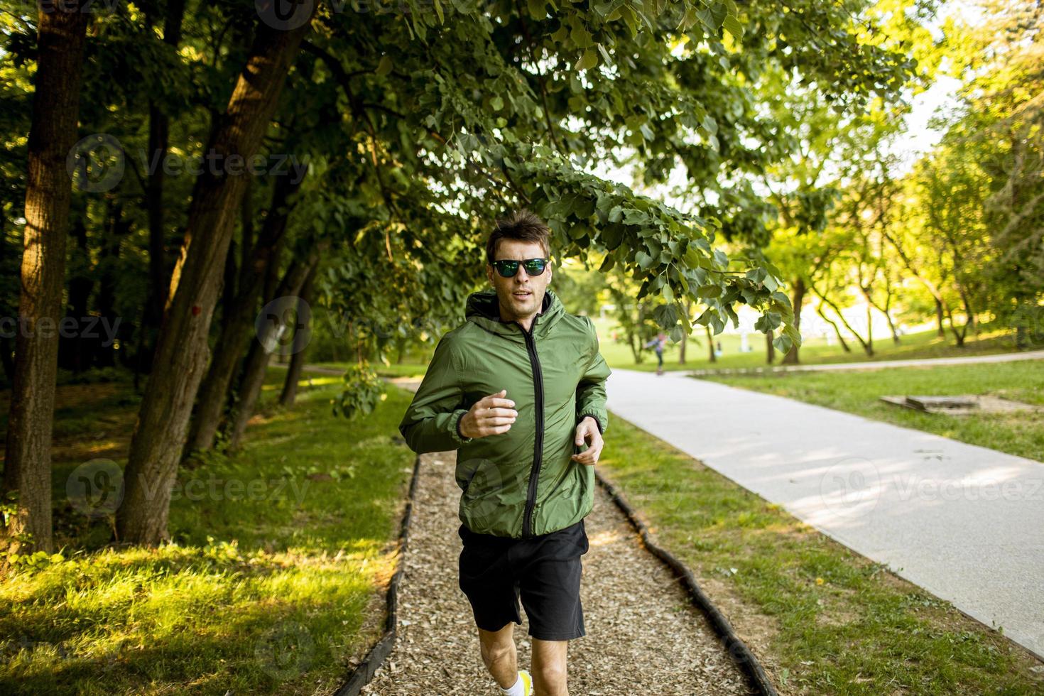 jovem atlético correndo enquanto faz exercícios no parque verde ensolarado foto
