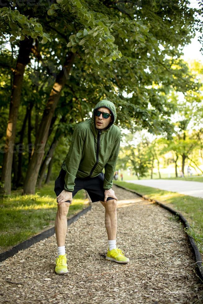 jovem atlético fazendo uma pausa enquanto se exercita no ensolarado parque verde foto