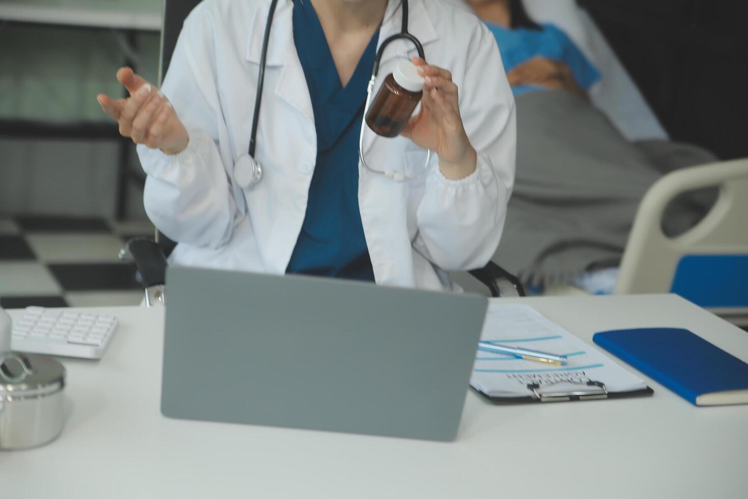 uma lindo e profissional ásia fêmea médico é trabalhando em dela médico casos em dela computador portátil ou fazer uma ligar médico consulta com uma paciente enquanto sentado dentro dela escritório. foto