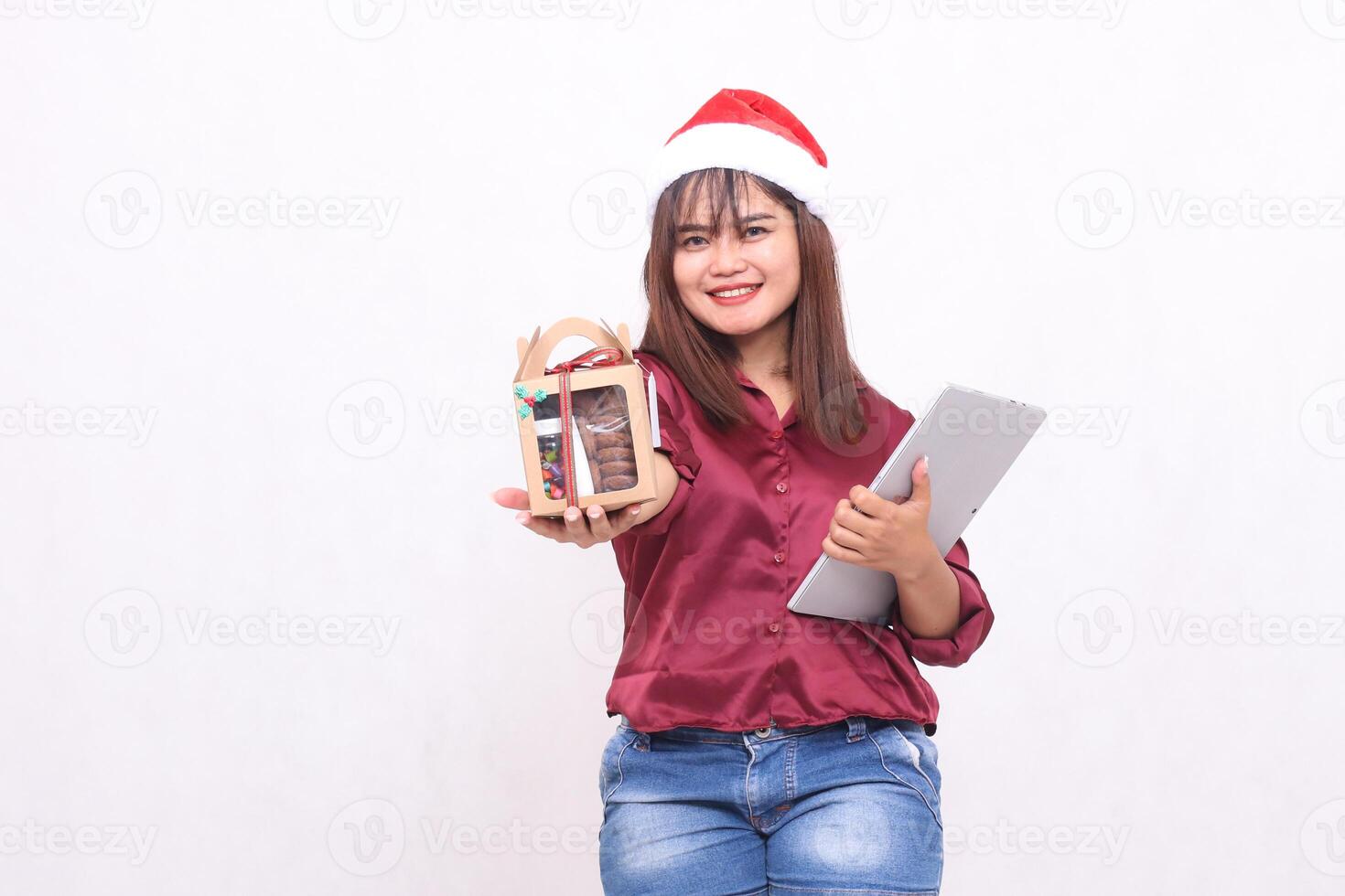 alegre jovem lindo sudeste ásia mulher dando presentes Comida pacote dentro dificultar e computador portátil tábua às Natal vestindo santa chapéu vestindo vermelho camisa moderno branco fundo para promoção, publicidade foto