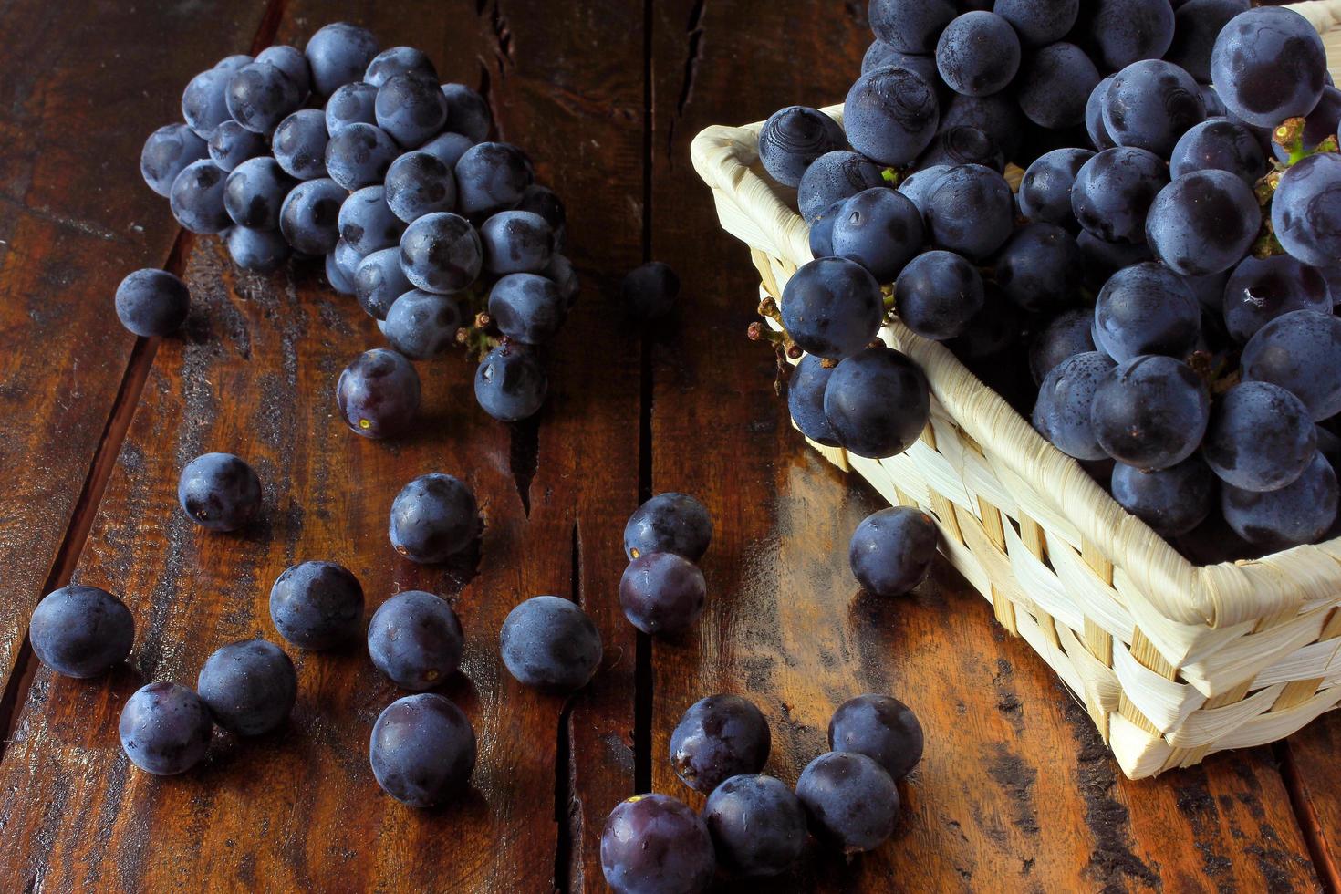 cachos de uvas, dentro de uma cesta de fibra de bambu na mesa de madeira foto