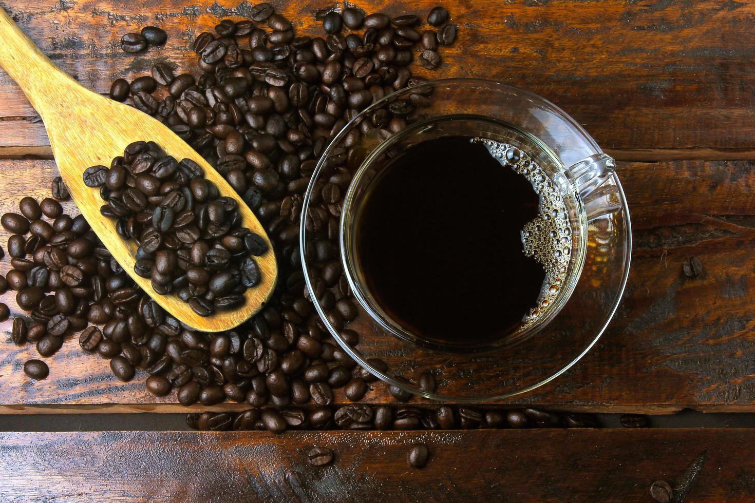 xícara com café fresco e grãos torrados derramados na mesa de madeira rústica foto