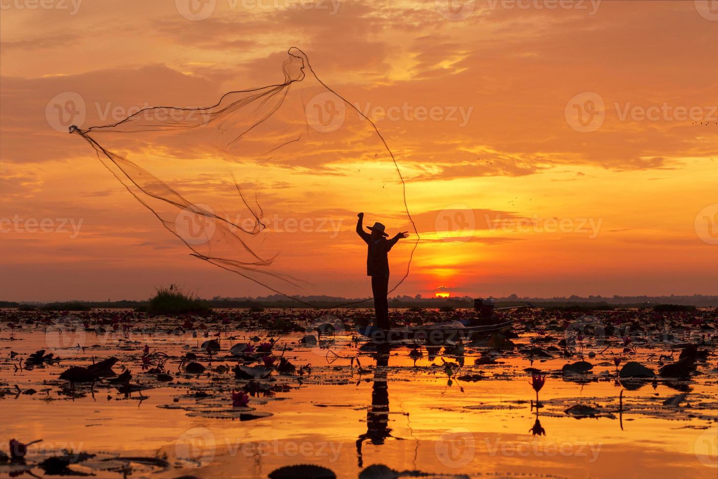 silhueta de rede de pesca este é um pescador em pé em um barco durante o nascer do sol no lago udon thani, na Tailândia. foto