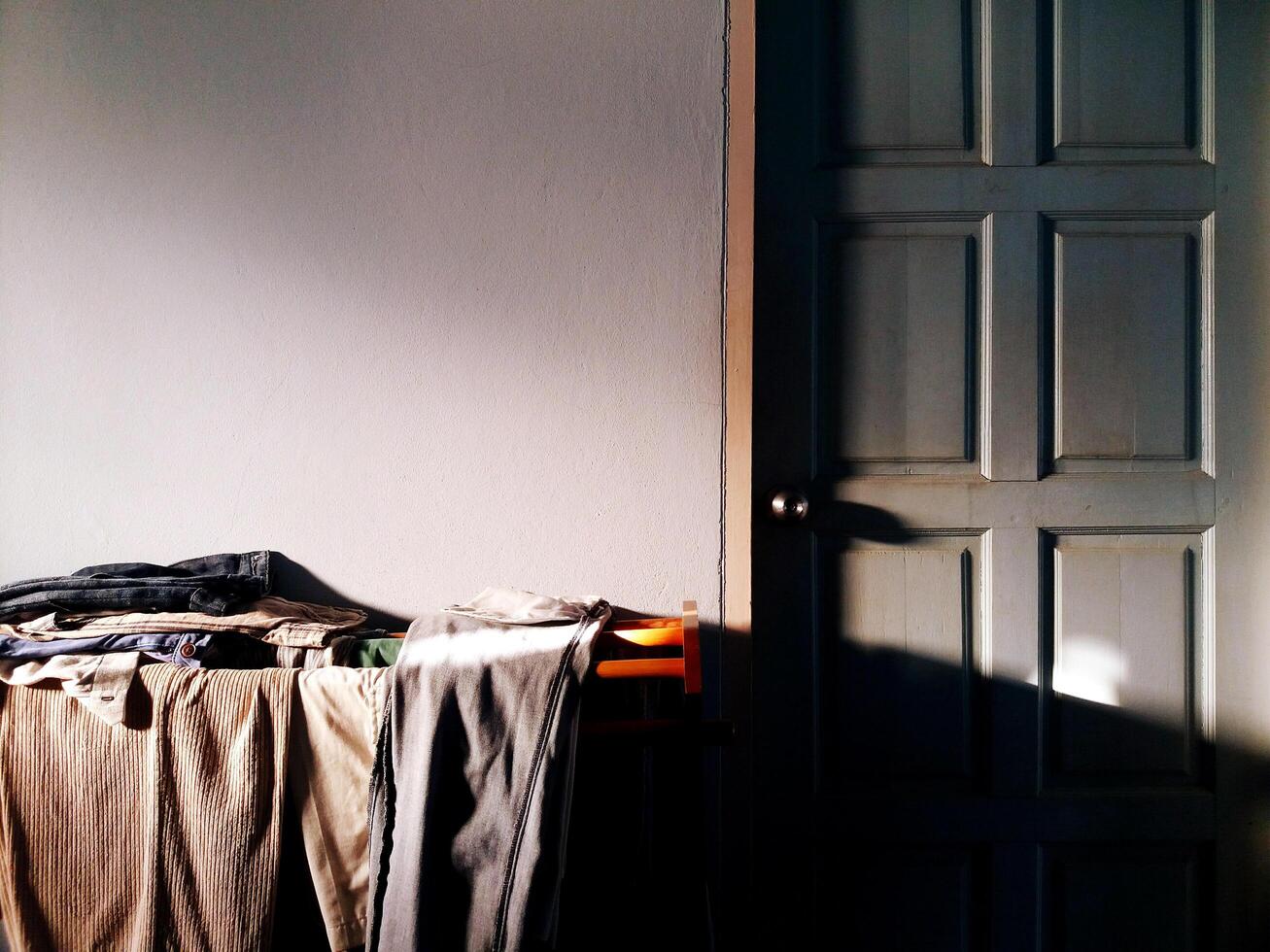 muitos roupas suspensão em a de madeira roupas linha ao lado a azul vintage porta com luz solar em a lado e cópia de espaço. dentro a manhã com arte luz Projeto. foto