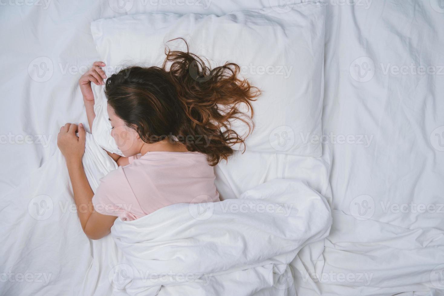 jovem dormindo bem na cama, abraçando o travesseiro branco macio. adolescente descansando. conceito de boa noite de sono. garota de pijama dorme em uma cama em um quarto branco pela manhã. tom quente. foto