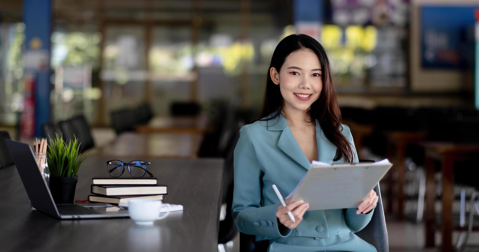 jovem mulher de negócios asiáticos lindo encantador sorrindo sentado trabalhando no escritório. olhando para a câmera. foto