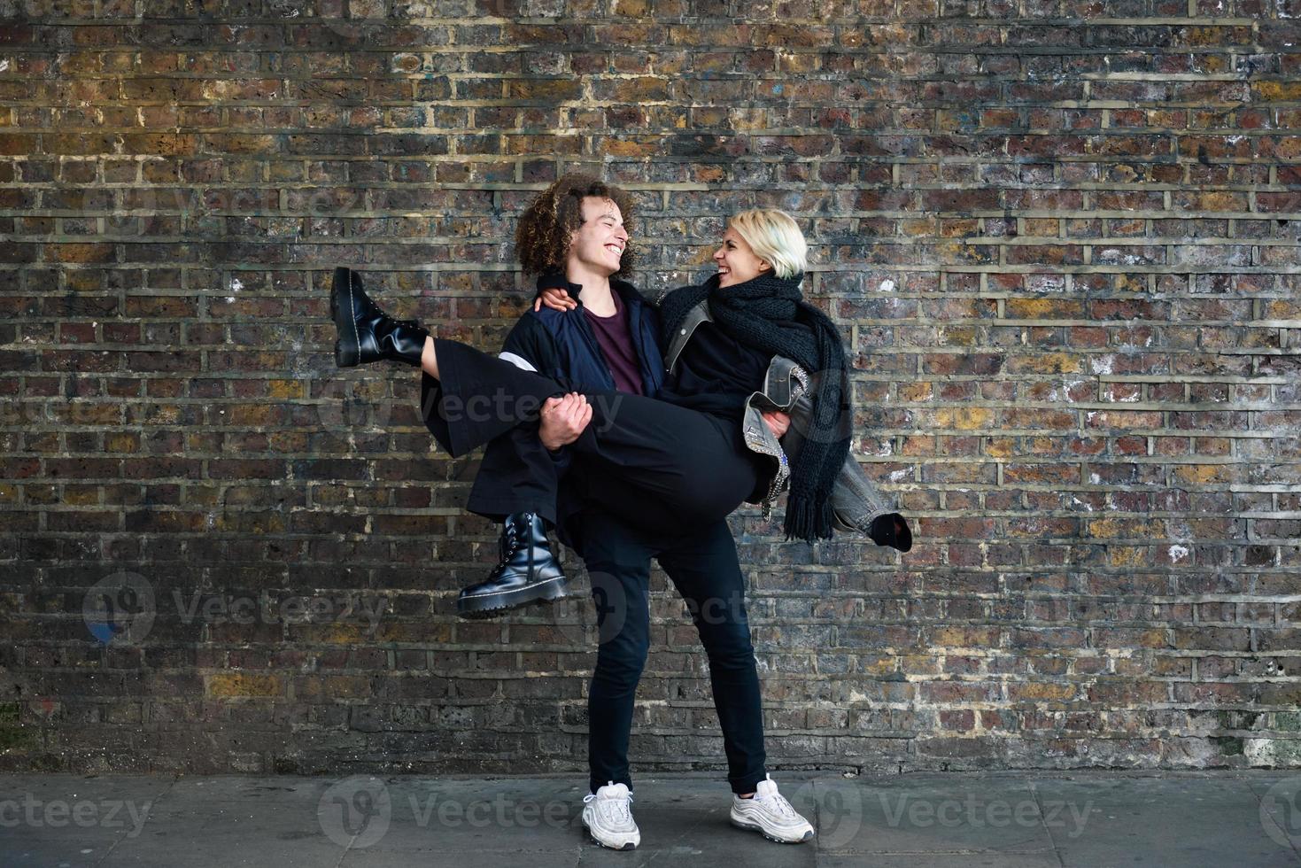 homem segurando a namorada nos braços em frente a uma parede de tijolos típica de Londres foto