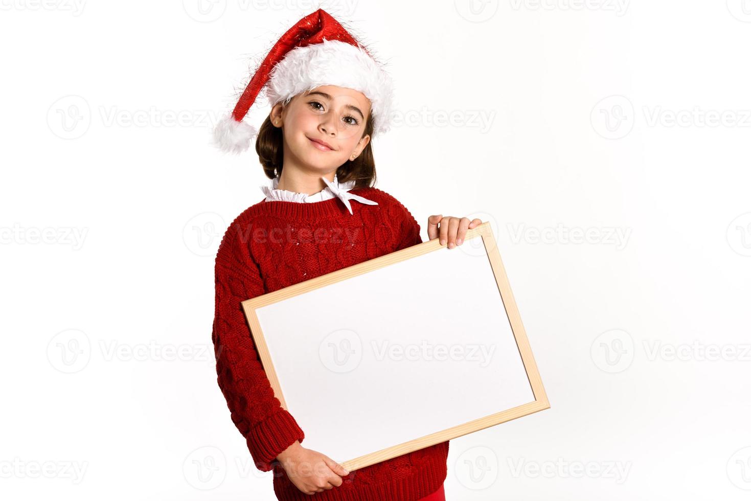 menina com chapéu de Papai Noel segurando um quadro em branco foto