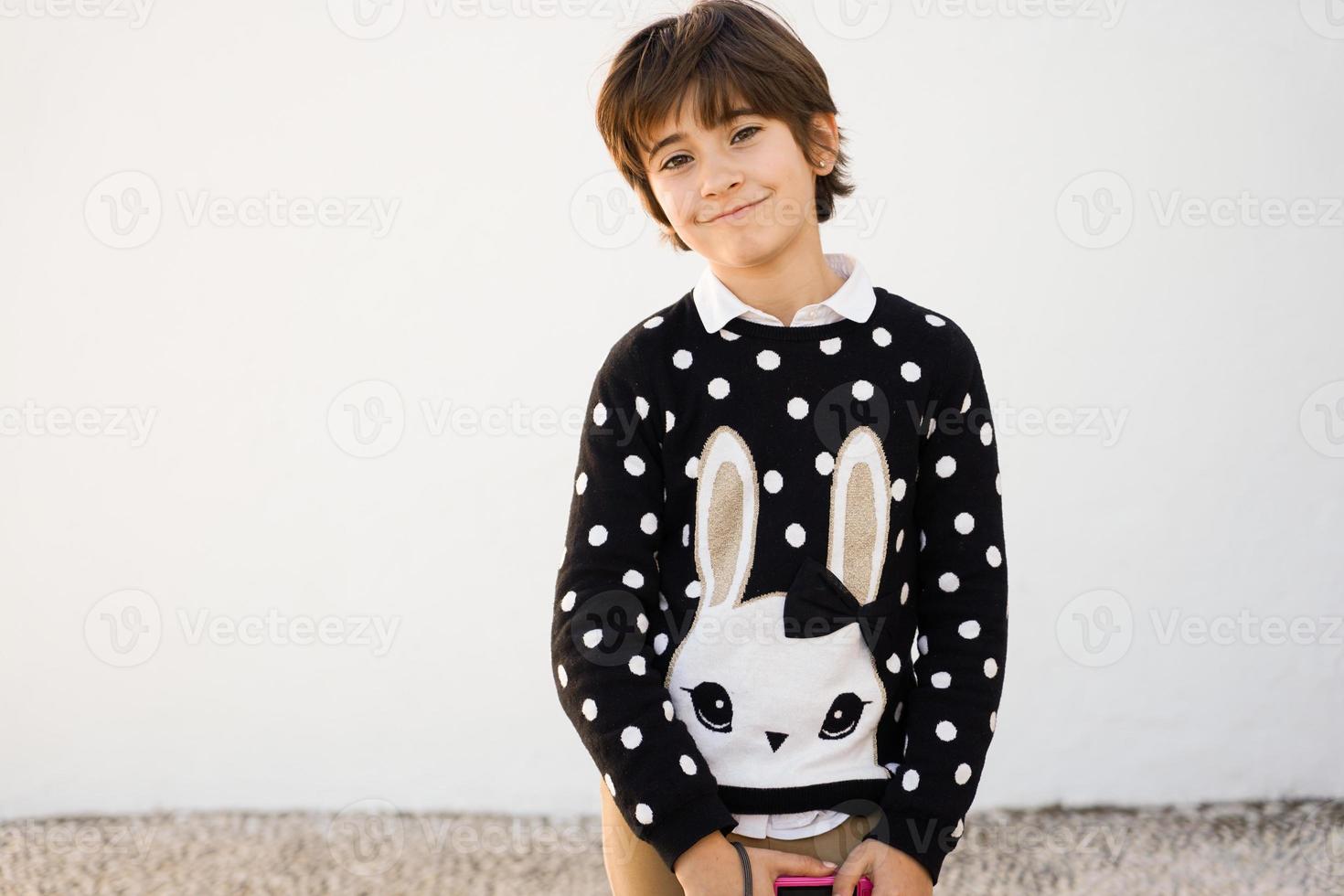 menina de sete anos com cabelo curto sorrindo em uma parede branca foto
